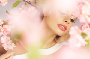 Woman in makeup with red lipstick, viewed through cluster of flowering tree branches